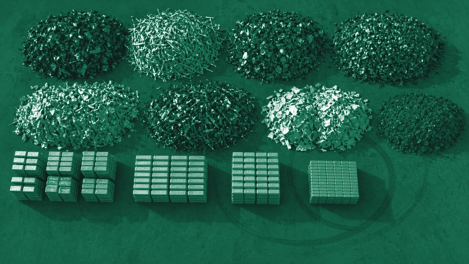 Top-down aerial view of a recycling yard with piles of sorted aluminium scrap and stacked ingots on concrete.