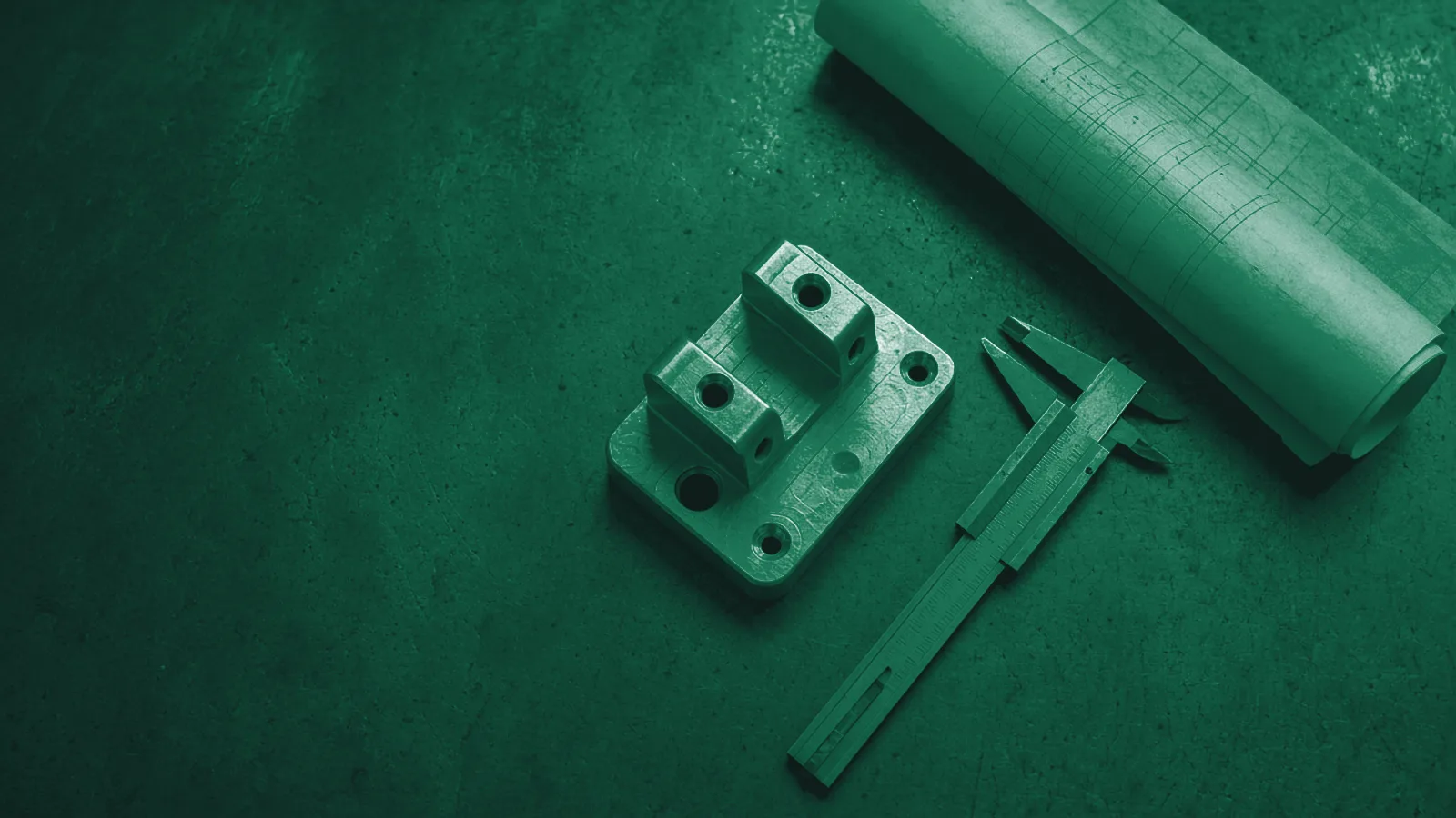 Top-down view of a steel inspection table with a machined aluminium part, a vernier caliper and a rolled technical drawing.